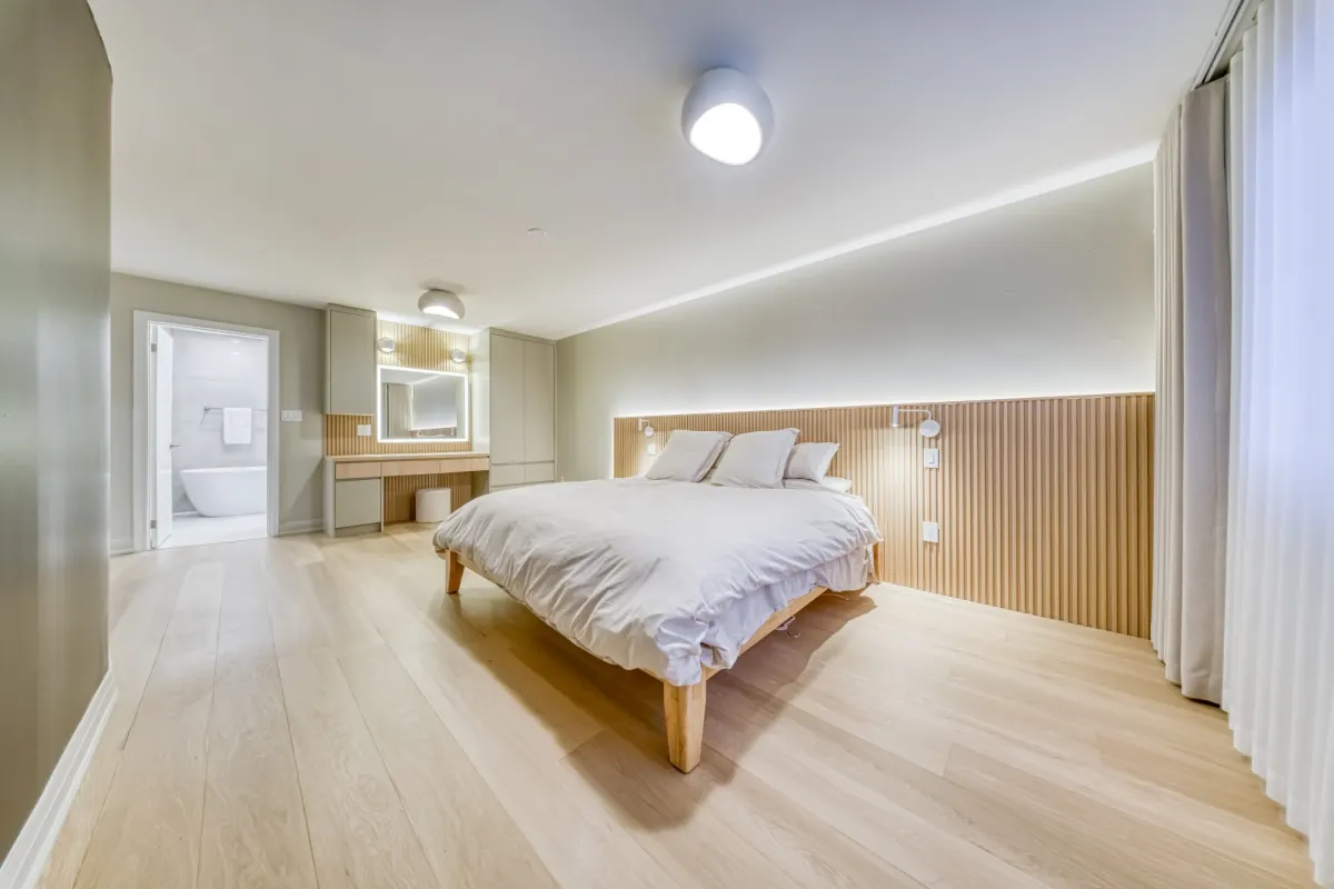 The primary bedroom: a slatted oak wall behind the bed and a lit vanity, with the ensuite beyond.