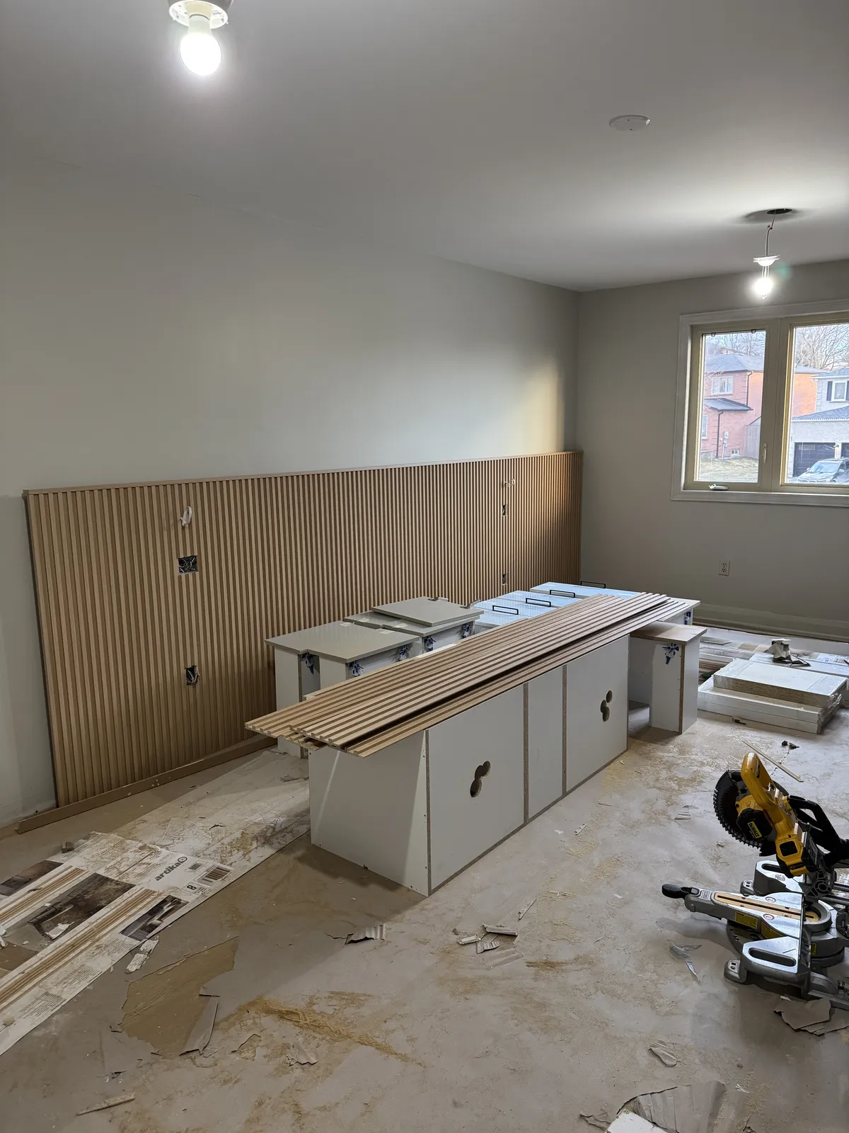 The primary bedroom mid-renovation: the slatted oak wall going up and cabinets waiting on the floor.