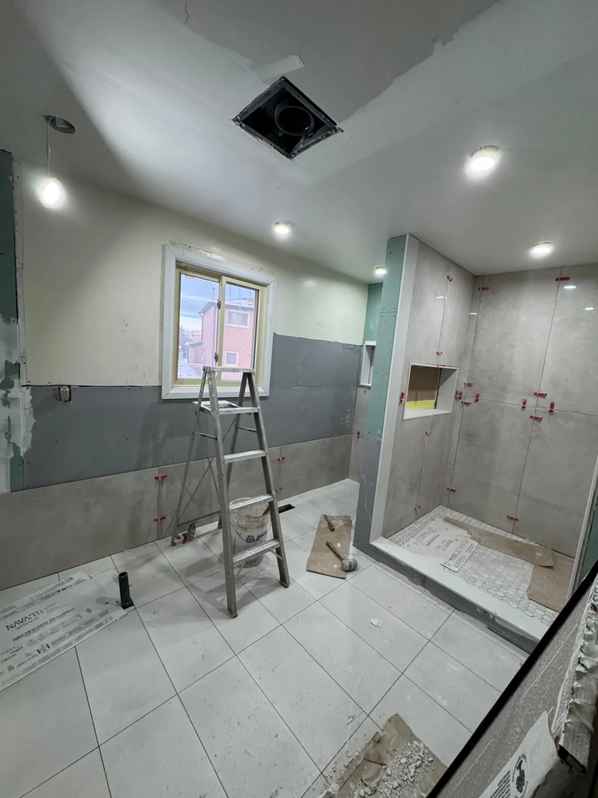 The ensuite mid-renovation: large grey tile going up with levelling clips and a new shower base.