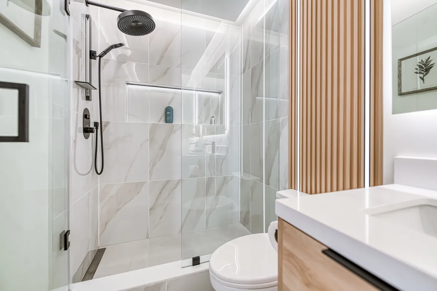 The finished shower: marble tile behind glass, beside an oak vanity.