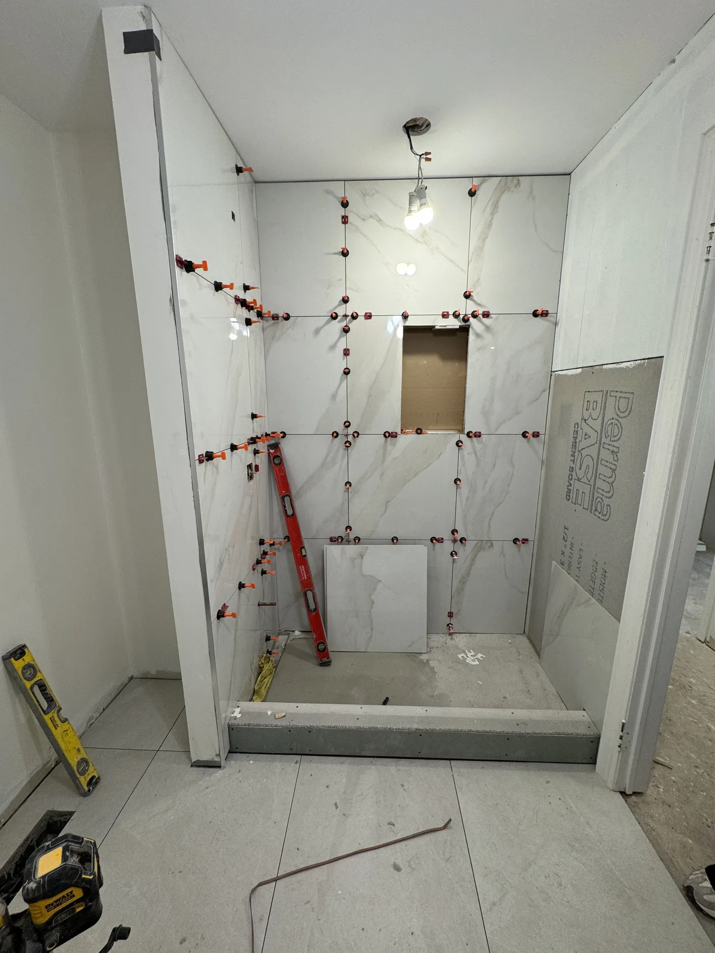 The shower mid-renovation: large marble tile going up with levelling clips.