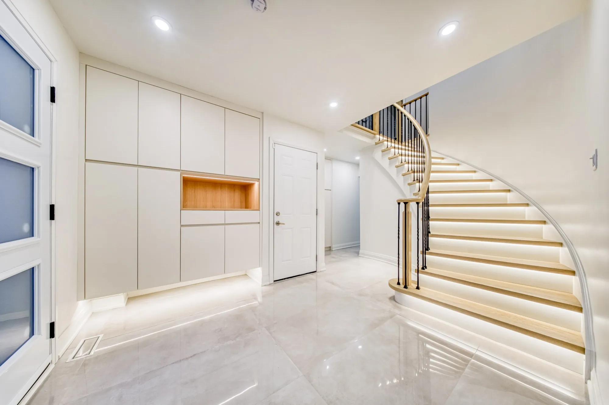 The finished entry: the same staircase with lit oak treads, iron spindles and a wall of built-in storage.